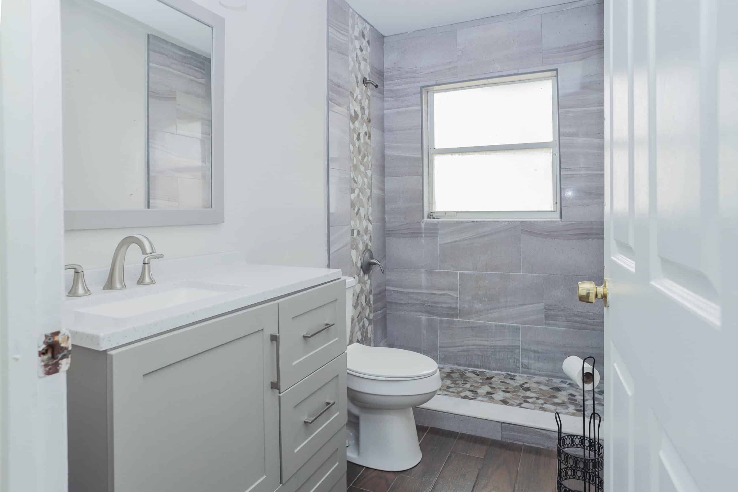 A modern bathroom with a vanity, toilet, and shower with gray tiles.