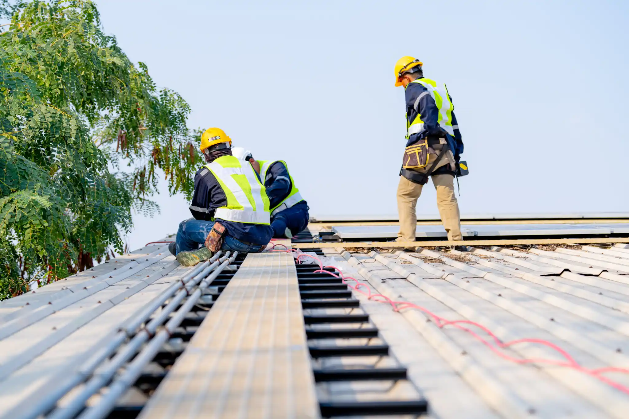 Workers installing solar panels on a roof under a clear sky.