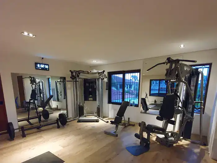 Home gym with various exercise machines, mirrors, and windows.