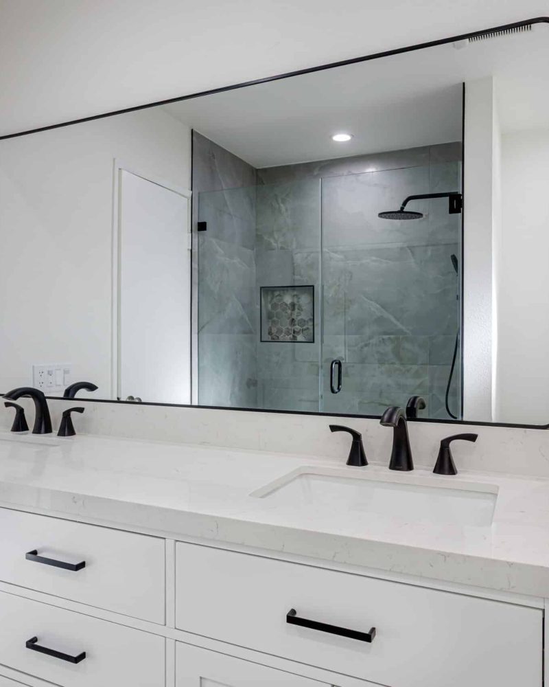 Modern bathroom with a large mirror, double vanity, and shower visible in reflection.
