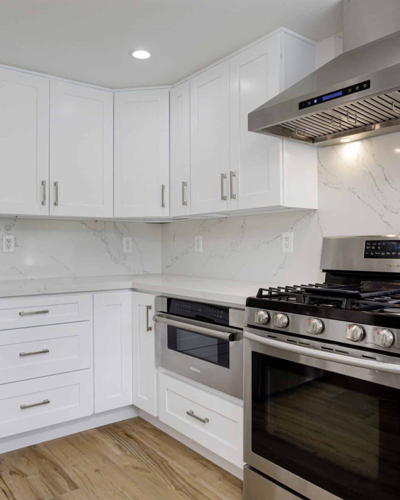Modern white kitchen with stainless steel appliances and wood floor.