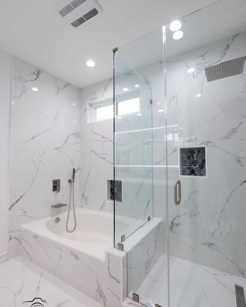 Modern bathroom with white marble walls, a bathtub, and a glass shower.