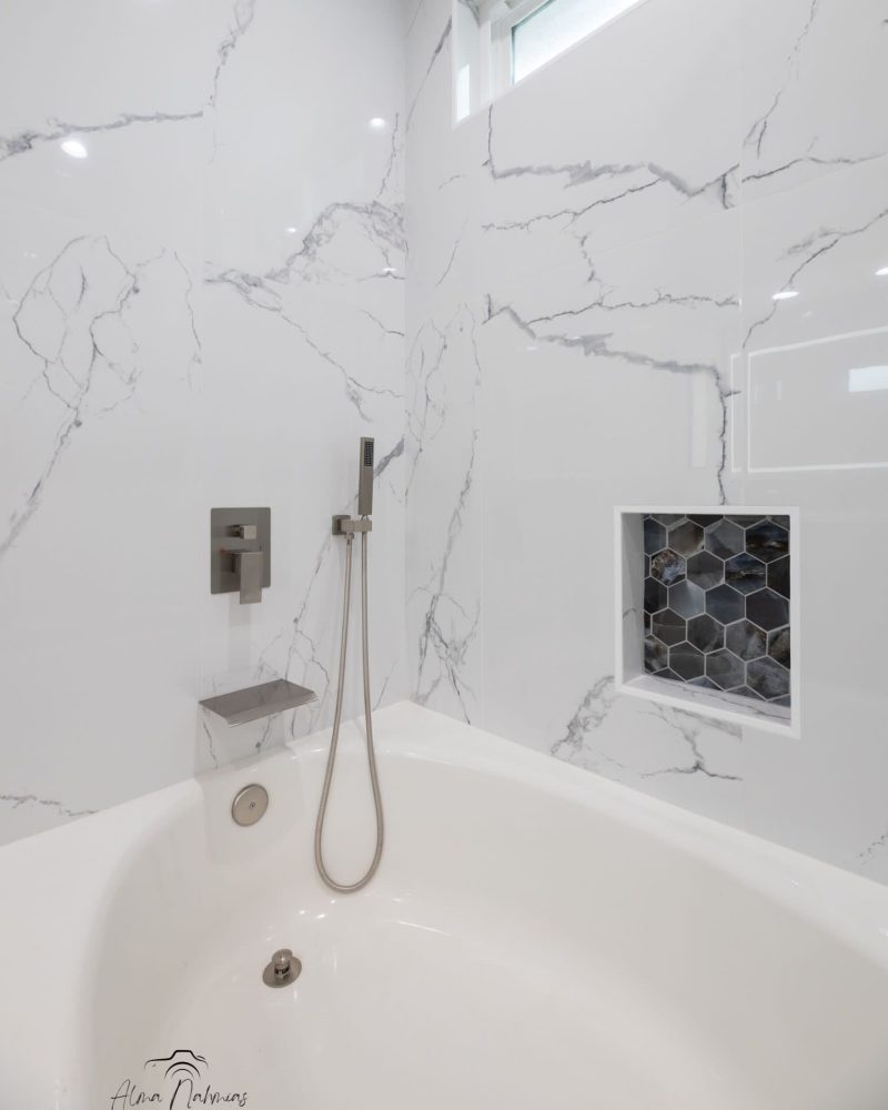 White bathtub with marble-patterned walls and a shower head