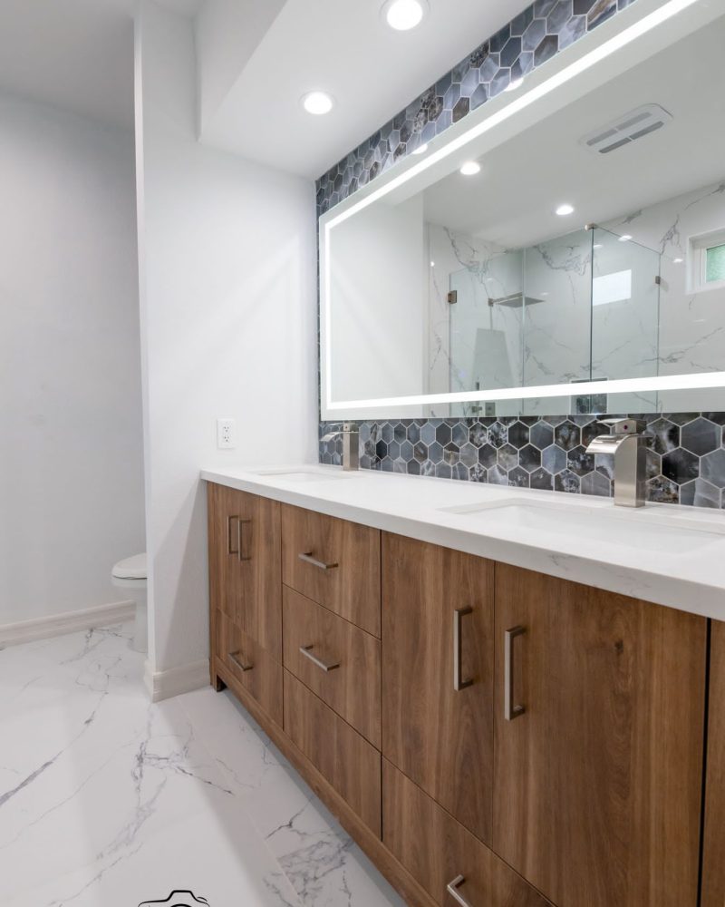 Modern bathroom with double vanity, illuminated mirror, and hexagonal tile backsplash.