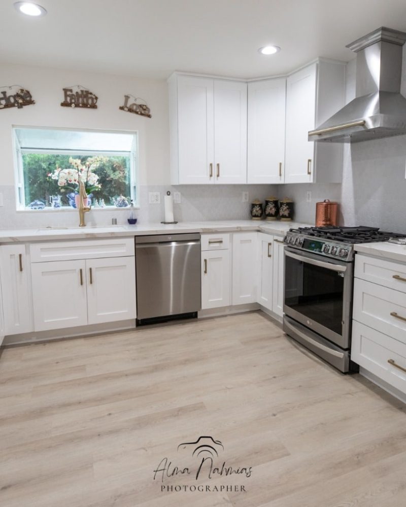 Modern white kitchen with stainless steel appliances and light wood floor.