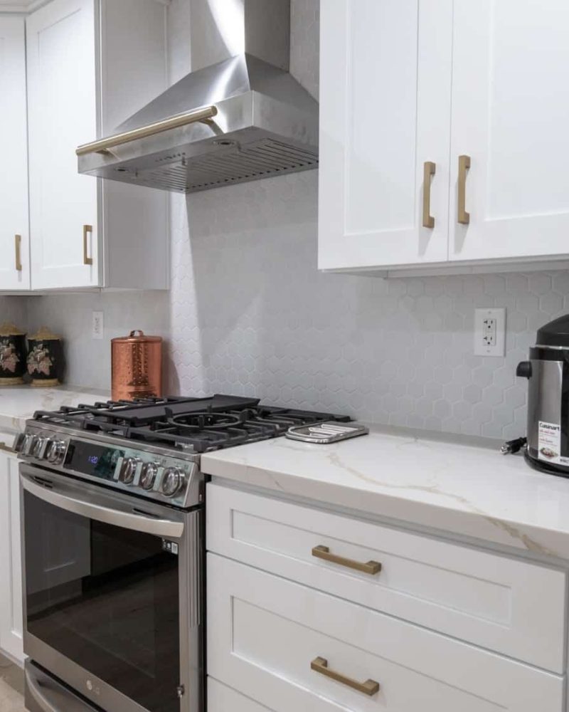 Modern white kitchen with stainless steel appliances and honeycomb tile backsplash.