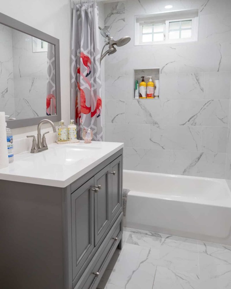 Bathroom with gray vanity, white marble tiles, and flamingo shower curtain.
