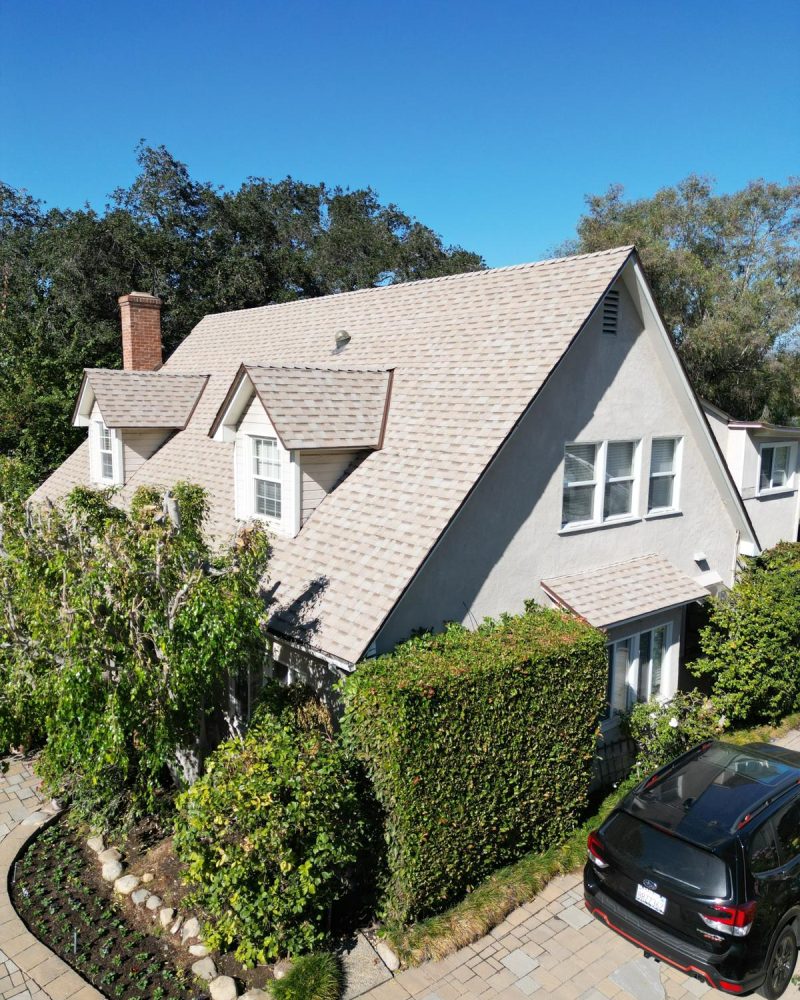 Aerial view of a house with a light-colored roof and surrounding greenery.
