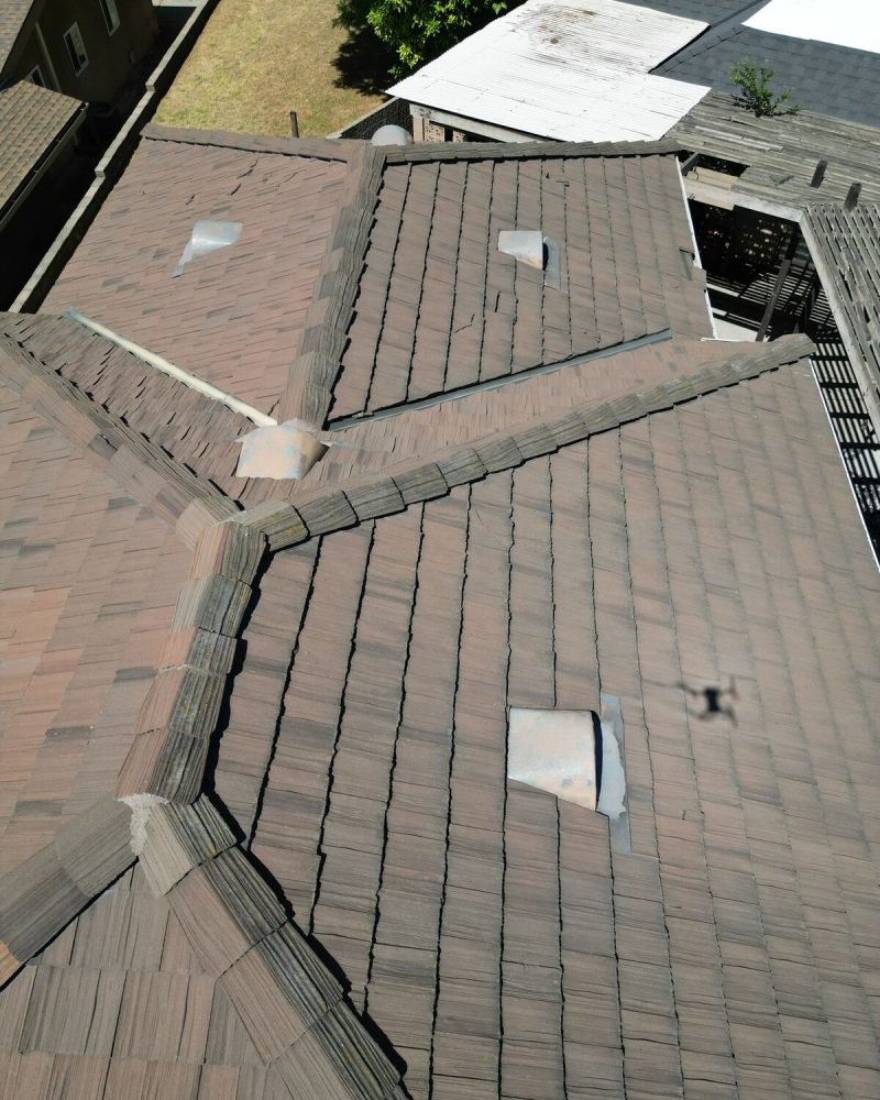 Aerial view of a brown shingle roof with vents and shadows