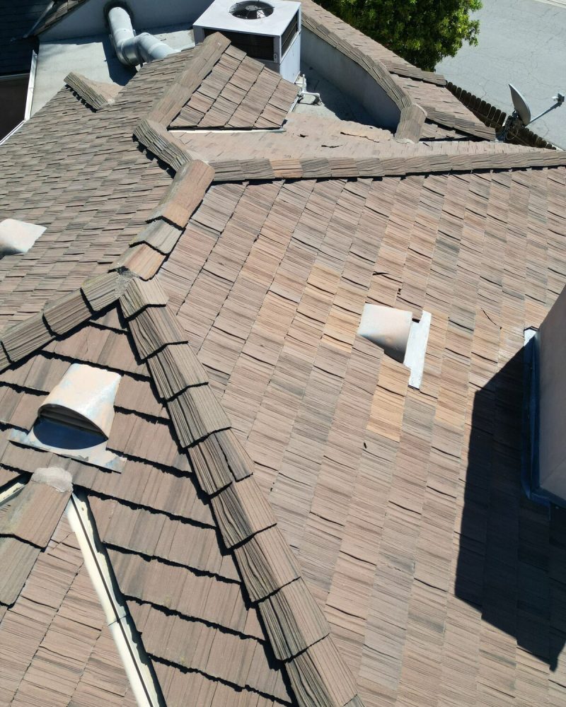 Aerial view of a brown shingle roof with vents and an AC unit.