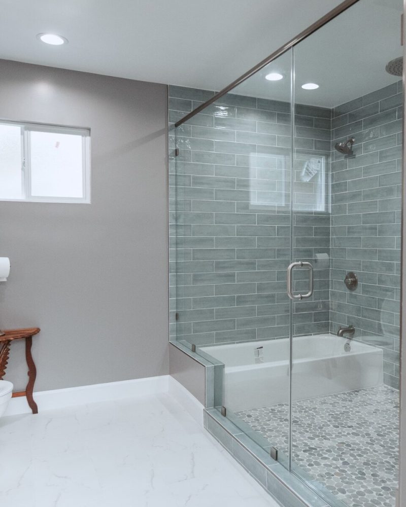 Modern bathroom with glass shower, bathtub, toilet, and small window.
