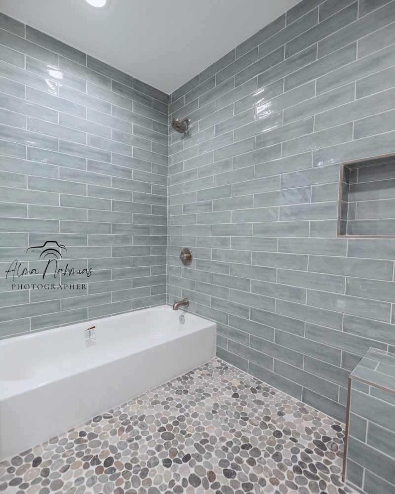 Modern bathroom with light blue subway tiles, a white tub, and pebble floor.
