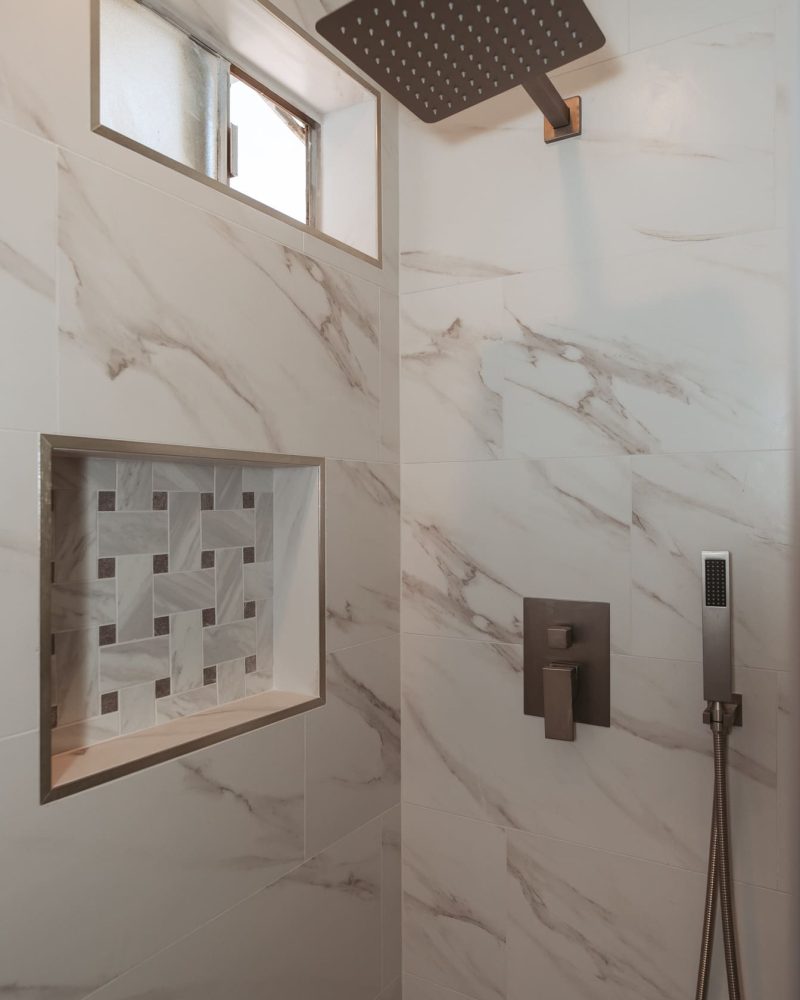 Modern shower with white marble tiles, rain showerhead, and handheld sprayer.