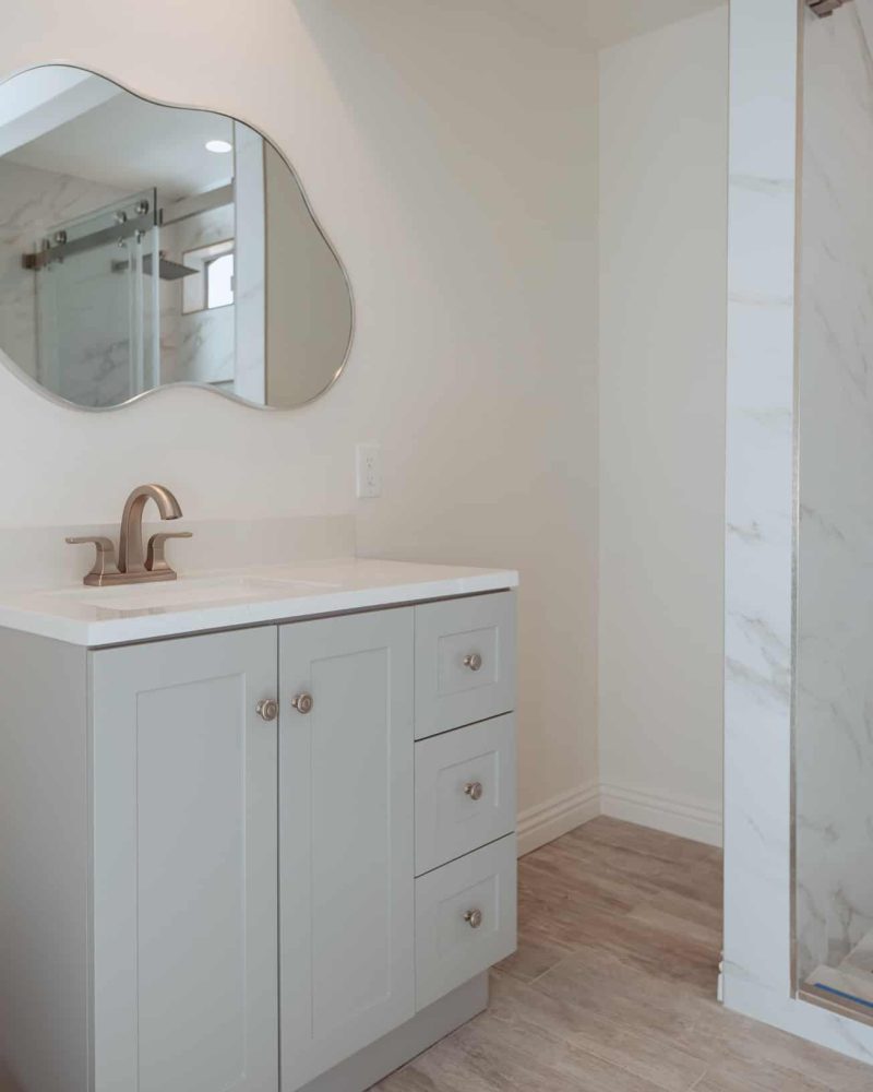 Modern bathroom with light gray vanity, unique mirror, and shower.