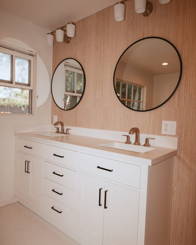 Modern bathroom with double vanity, round mirrors, and wood-paneled wall.