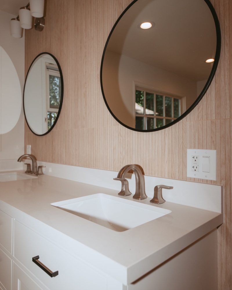 Modern bathroom with two sinks, two round mirrors, and wood-paneled wall.