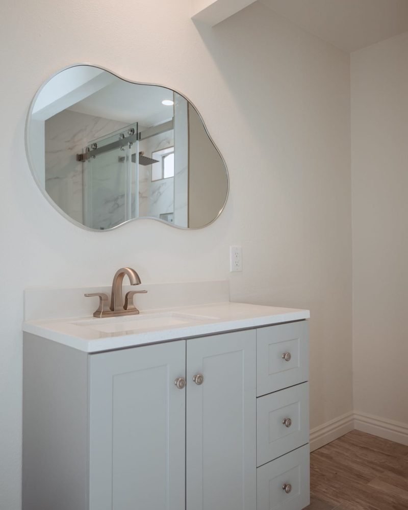 Modern bathroom vanity with a unique mirror and light gray cabinets.