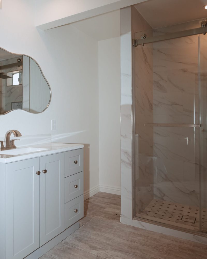 Modern bathroom with white vanity, unique mirror, and glass shower.
