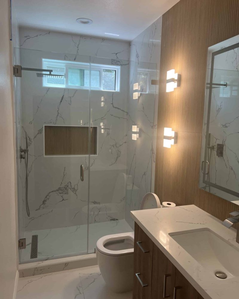 Modern bathroom with glass shower, marble tiles, and wooden accents.