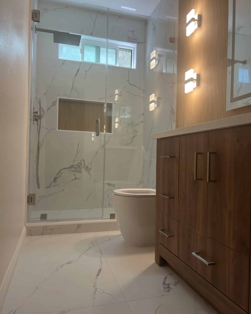 Modern bathroom with glass shower, toilet, and wooden vanity.