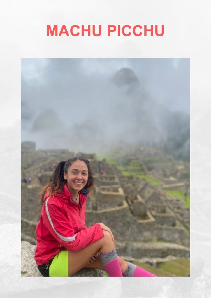 Spiritual Places in Peru That Aren't Machu Picchu! The young woman aka Giorgy in a pink jacket and bright shorts sits on an ancient stone ledge with the iconic ruins of Machu Picchu shrouded in mist in the background.