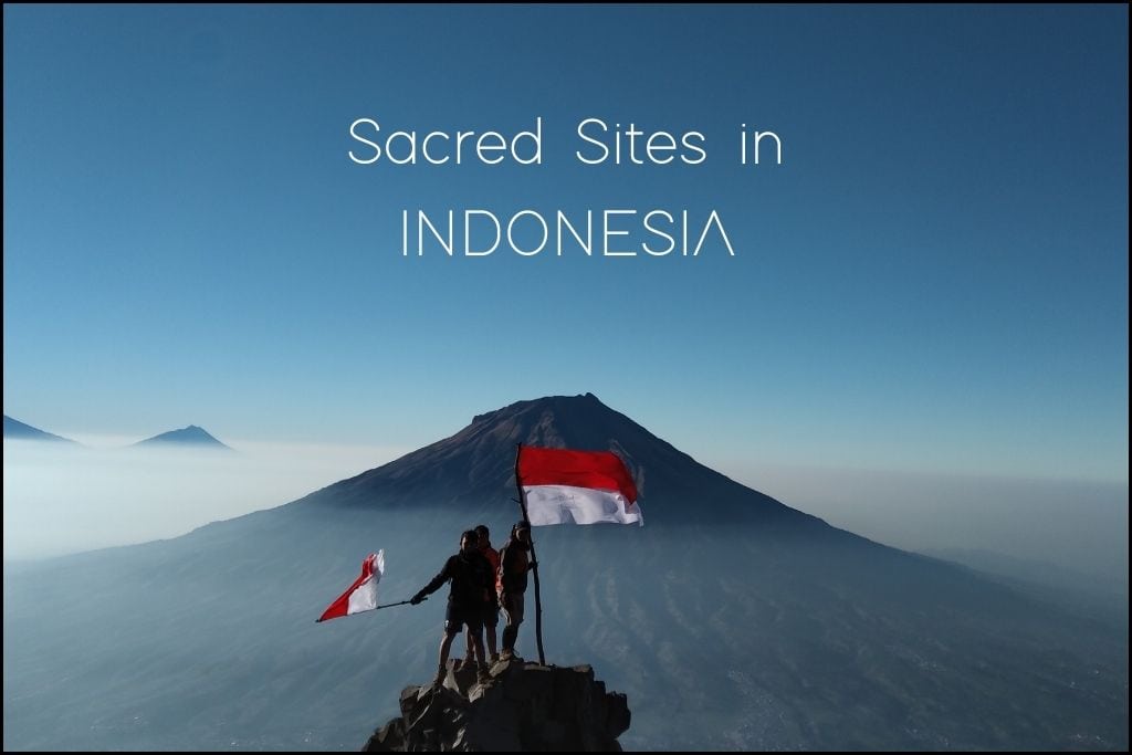 Two hikers stand triumphantly atop a mountain ridge in Indonesia, with 'Sacred Sites in INDONESIA' floating above them in the sky. They are holding the Indonesian flag, with the sun casting a soft light on the volcanic landscape and the misty horizon stretching out behind them.