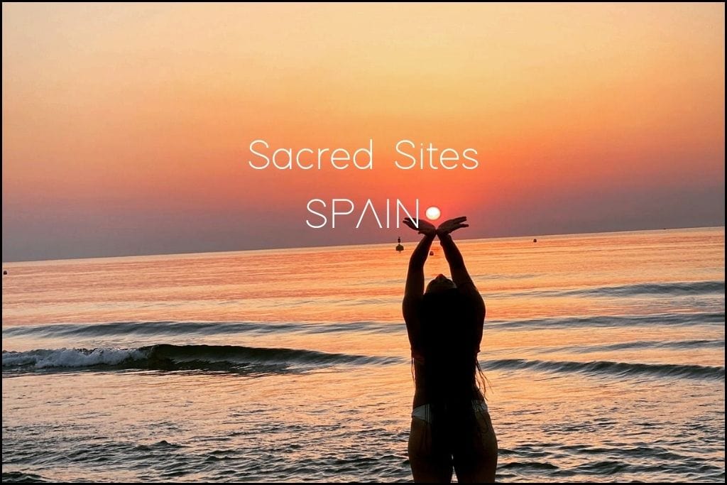 A silhouette of Giorgy with arms raised captures the sun between their hands at sunset on a tranquil Spanish beach, the sky painted in hues of deep orange and purple. 'Sacred Sites in SPAIN' hints at a journey through Spain's serene landscapes and their spiritual significance.