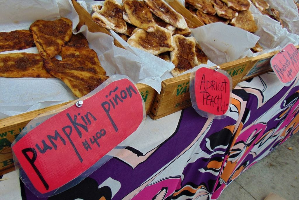 Your Guide to Santa Fe Spiritual Vortex in 2026 Handmade pastries on display at a market, with tags indicating 'Pumpkin Piñon' and 'Apricot Peach', set against a colorful tablecloth. Your Guide to Santa Fe Spiritual Vortex in 2025