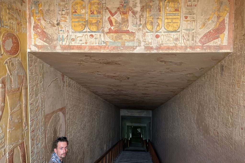 Visitors entering a tomb at the Valley of the Kings in Luxor, Egypt, with walls adorned with ancient hieroglyphs and vibrant Egyptian artwork, showcasing a rich tapestry of historical storytelling.