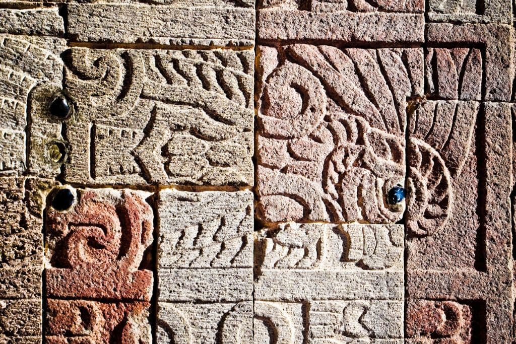 Your 2026 Spiritual Guide to The Pyramids of Teotihuacan Close-up of an ancient wall with intricate carvings and hieroglyphics in beige and pink tones, showcasing traditional patterns and symbolic designs.