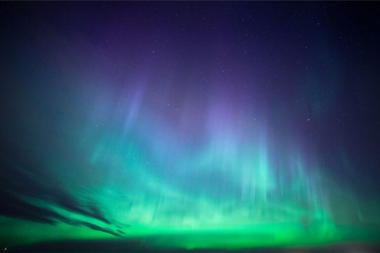 A stunning display of the Aurora Borealis with vivid green and purple lights cascading across the starlit night sky.
