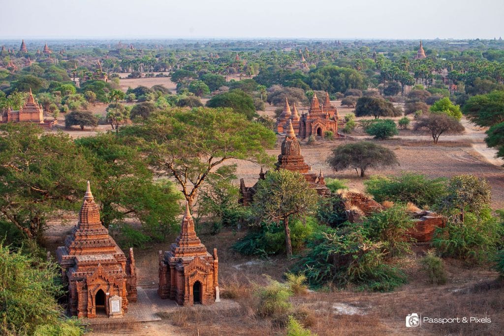 Is Bagan a Spiritual Place? Discover Why Should You Visit Bagan Myanmar in 2026! Elevated view of a cluster of ancient, smaller brick temples in the forested landscape of Bagan, Myanmar, illustrating a serene and historical scene.