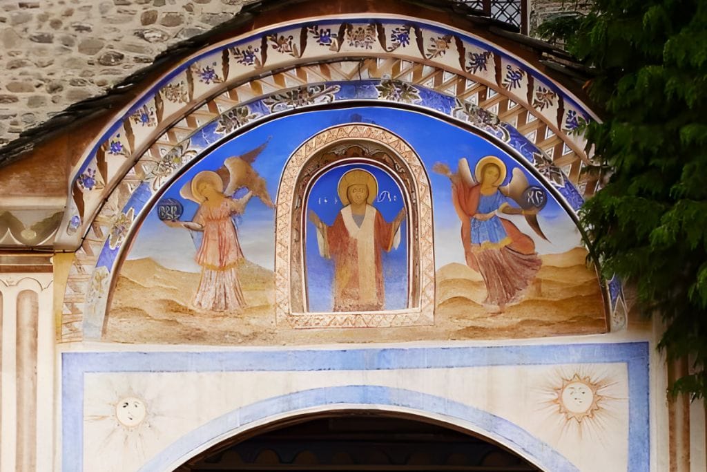 Rila Bulgaria Spiritual: The Most Spiritual Places to Visit in Bulgaria! An intricately painted archway at the Rila Monastery in Bulgaria, featuring religious frescoes with depictions of saints and angels. The arch leads into the monastery's courtyard, with stone walls and a serene atmosphere highlighting the historical and spiritual significance of this Eastern Orthodox site.