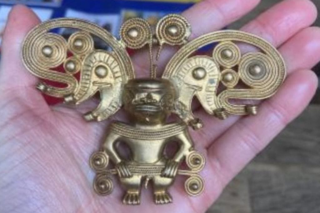 How to Get to the Lost City Colombia? My Personal Experience in 2026! A hand holding a golden figurine with elaborate design, possibly representing a deity or a ceremonial object, with various other artifacts displayed on a table in the background.