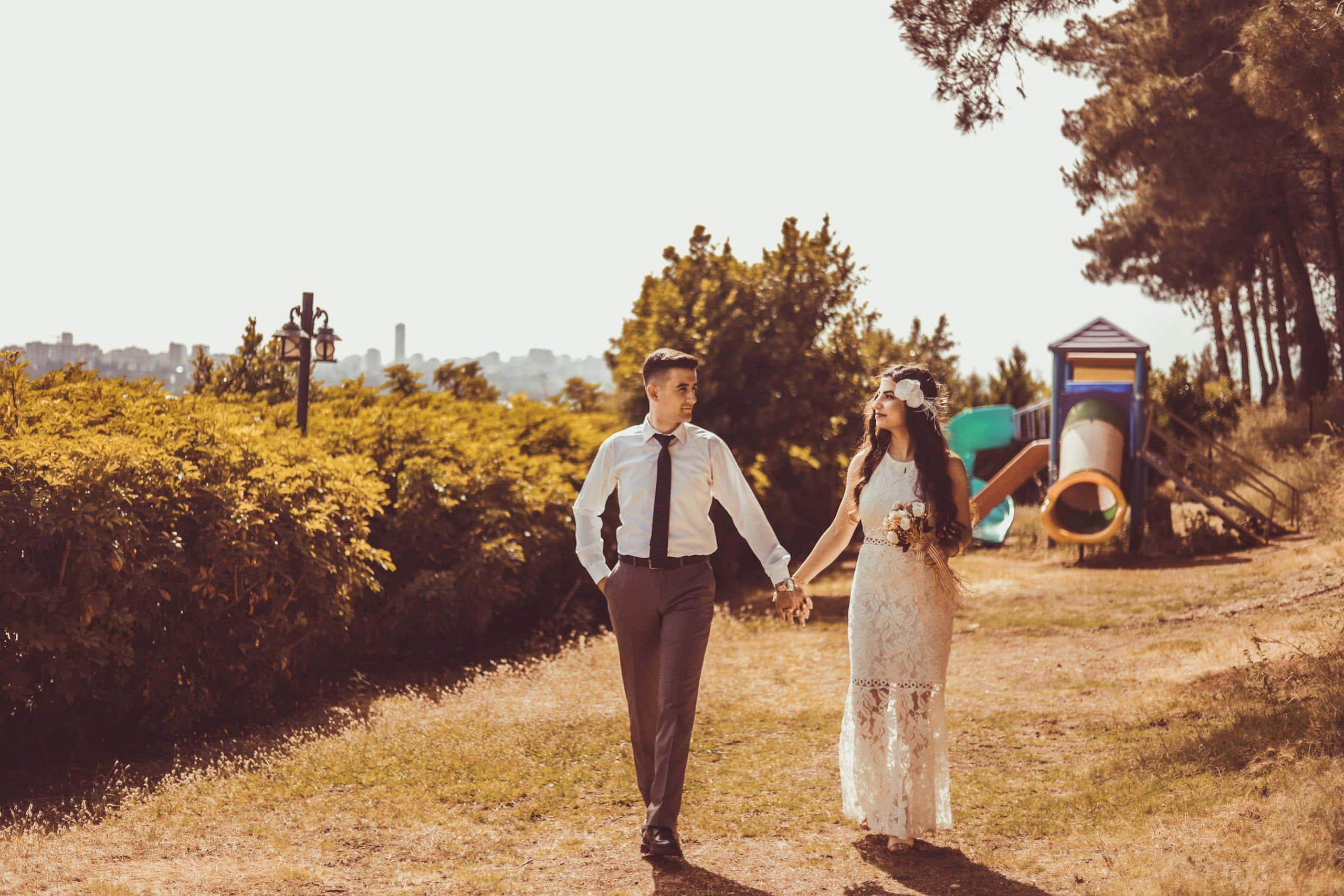 1110 Angel Number Meaning and Significance A photo of a couple holding hands while walking. They are seen from behind, strolling down a scenic path surrounded by trees and greenery. The couple's hands are clasped tightly, symbolizing their connection and affection. The background is softly blurred, emphasizing the intimacy and tranquility of the moment, showing Angel Number 1110 in love
