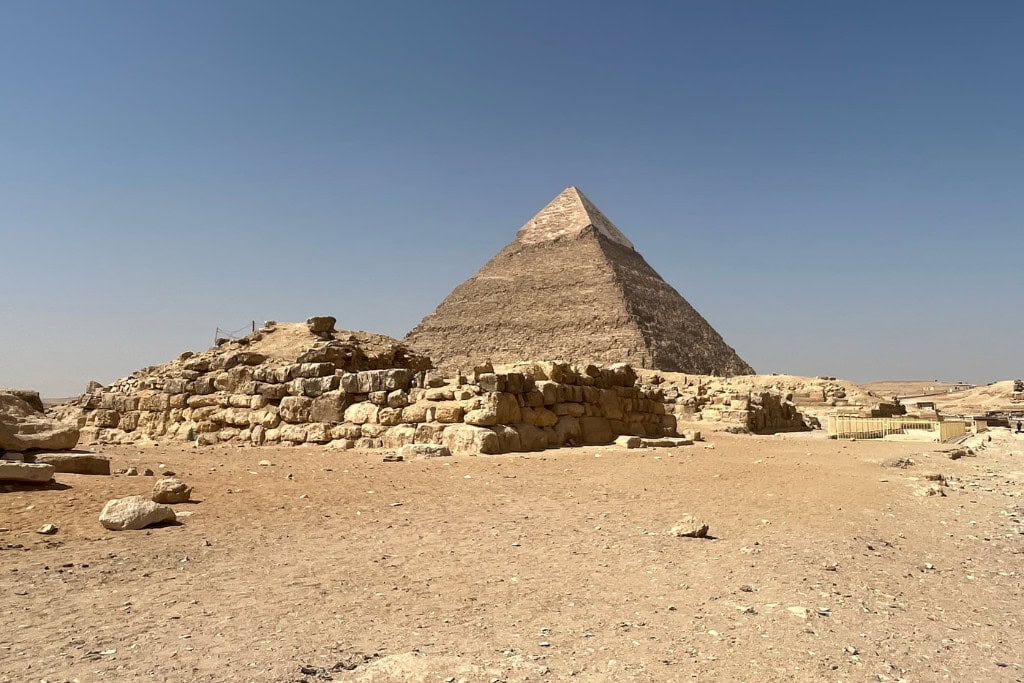 What Do Giza Pyramids Represent Spiritually? A view of the Great Pyramid of Giza, towering over the surrounding ancient stone structures under a clear blue sky. The image highlights the massive scale and precise geometry of the pyramid, representing the spiritual journey of the pharaoh's soul towards the heavens. The Giza Pyramids are deeply symbolic in ancient Egyptian belief, often interpreted as monuments of spiritual ascent and eternal life.