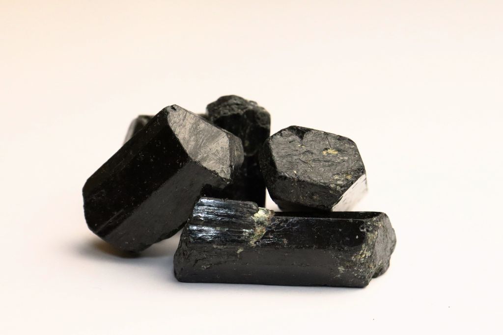 The image shows several dark, shiny crystals of black tourmaline arranged against a plain white background. The crystals have a hexagonal structure with rough edges, and they appear to reflect light, highlighting their glossy surface.