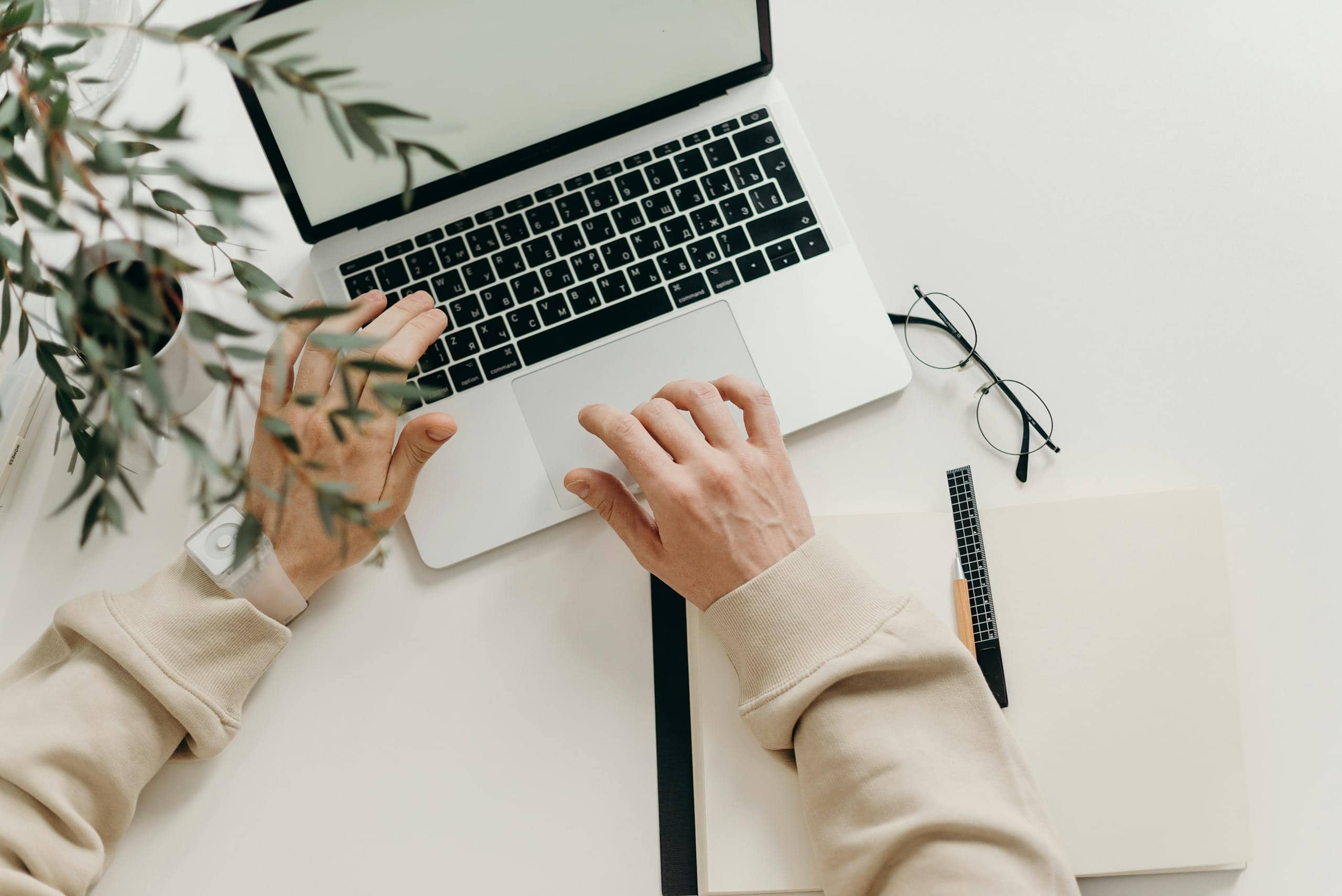 175 Angel Number - Meaning in Life Image of a person wearing a beige long sleeve shirt is seated at a desk, using a MacBook Pro. The laptop screen glows softly, with the person's hands resting on the keyboard, focused on their work in a calm, indoor setting.