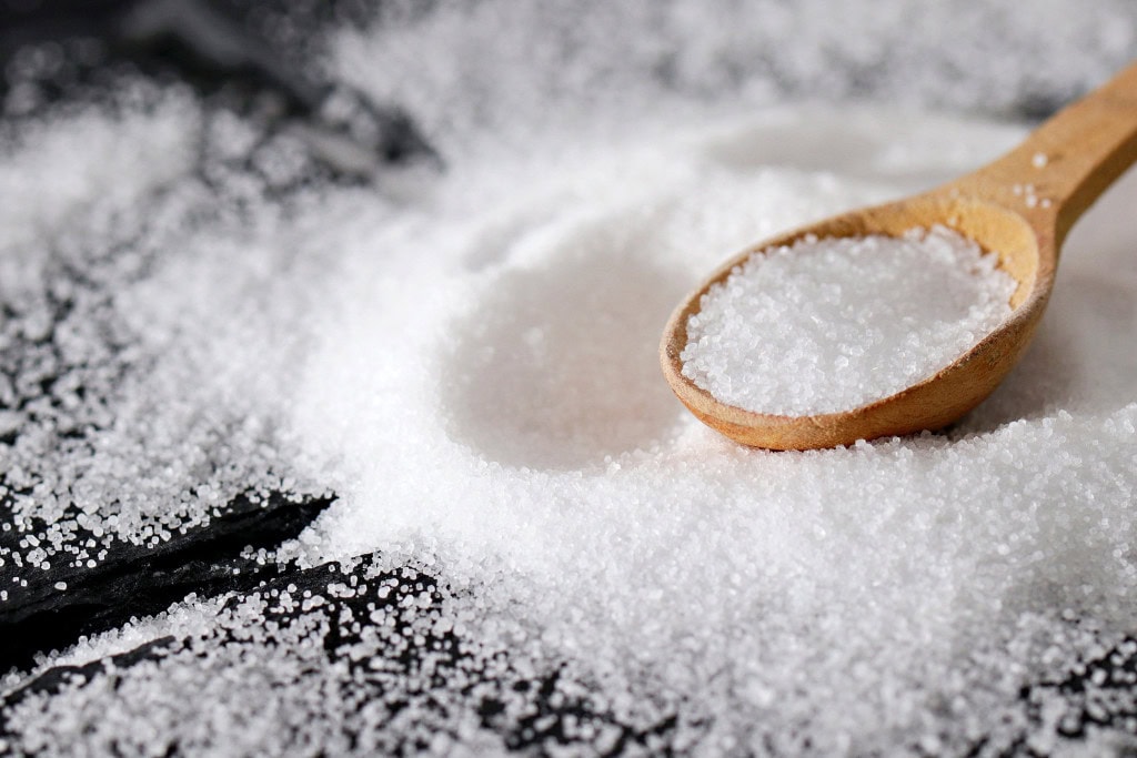 Cleansing Your House from Negative Energy: Everything You Need to Know! This image shows a wooden spoon resting on a pile of coarse white salt, with granules scattered across a dark surface. The texture of the salt is emphasized, and the scene evokes a sense of simplicity and natural ingredients, potentially symbolizing cooking or purification. The focus on the spoon suggests careful measurement or use of the salt.