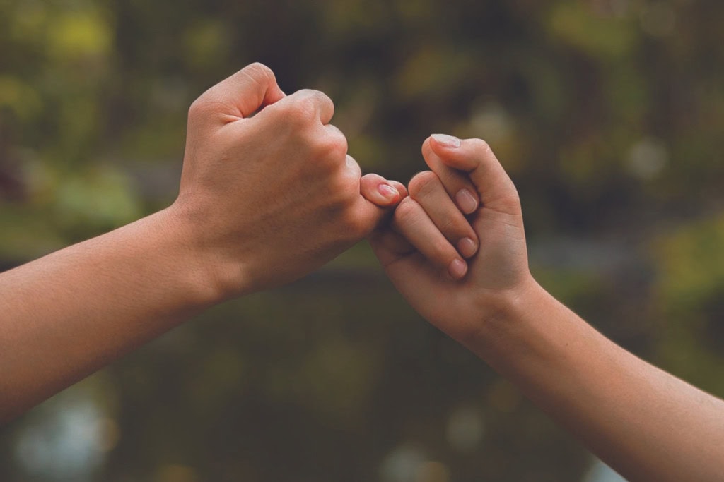 Cleansing Your House from Negative Energy: Everything You Need to Know! This image shows two hands linking pinky fingers in a gesture of promise or commitment, often referred to as a "pinky swear." The outdoor background is softly blurred, keeping the focus on the hands, symbolizing trust, loyalty, or a special bond between two individuals. The simplicity of the gesture emphasizes emotional connection.