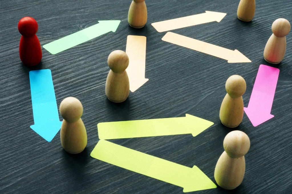 Cleansing Your House from Negative Energy: Everything You Need to Know! This image shows wooden figurines arranged on a dark surface with colorful arrows pointing in various directions between them. One figurine is painted red, standing out among the others. The arrows suggest communication, direction, or workflow, while the red figure might symbolize leadership, a key player, or an outlier in a network. The overall composition implies interaction, organization, or team dynamics.
