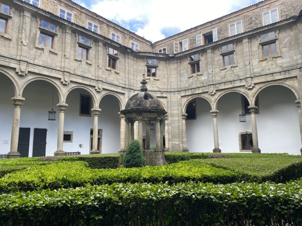 What is the spiritual meaning of Santiago de Compostela? The lush courtyard of the Parador in Santiago de Compostela, featuring manicured hedges, a central stone fountain, and arched colonnades that evoke the building's rich historical and architectural heritage.