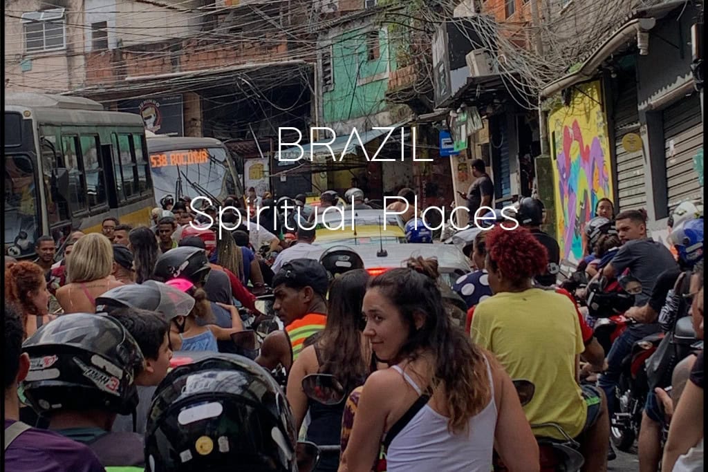 Find Your Spiritual Places in South America This image shows a crowded urban street scene in Brazil with a mix of motorcycles, pedestrians, and buses against the backdrop of tightly packed buildings and vibrant street art. The text overlay reads "Brazil Spiritual Places," suggesting a thematic connection between the location and spirituality.