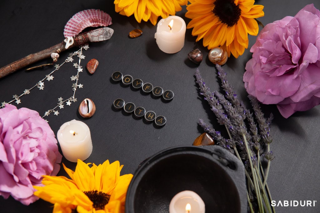 The Celtic Wheel With Sabiduri: Walk in the Truth A vibrant Litha altar celebrating the Celtic Wheel, adorned with sunflowers, lavender sprigs, pink roses, and glowing candles on a dark background. The words 'Joyful Litha' are spelled out in lettered beads, surrounded by a cauldron, seashells, crystals, and a wand decorated with star-shaped charms. This sacred setup honors the summer solstice, symbolizing abundance, light, and the peak of the sun’s power.