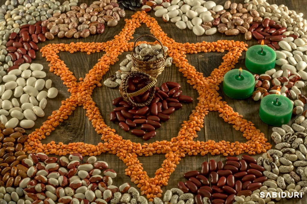 The Celtic Wheel With Sabiduri: Walk in the Truth A Lammas altar honoring the Celtic Wheel, featuring a sacred geometric design made from lentils, beans, and seeds, symbolizing the first harvest. At the center, a small basket overflows with grains and legumes, representing abundance and gratitude, while three green candles burn nearby. This earthy and nourishing setup reflects the spirit of Lammas, a festival celebrating the bounty of the land and the turning of the seasons.