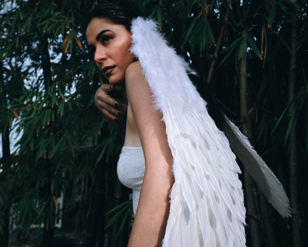 Why You Keep Seeing Angel Number 8 Everywhere? Woman dressed as an angel with white feathered wings, standing among tall bamboo, evoking themes of divine guidance and the presence of Angel Number 8.