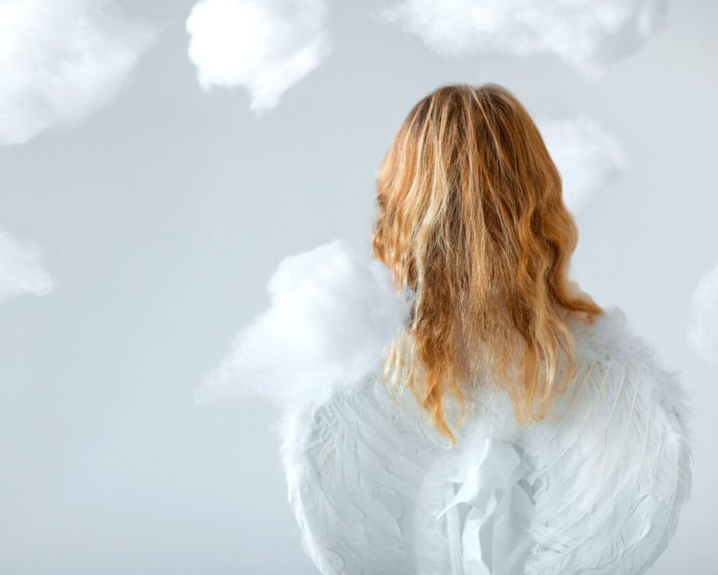 Discover the Spiritual Meaning of Angel Numbers 9 A woman with golden hair and angel wings stands among clouds, gazing upward, symbolizing faith, clarity, and the spiritual meaning of angel numbers 9.
