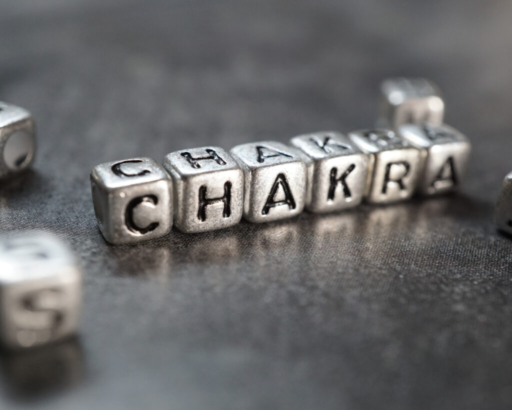 Close-up of metallic letter beads spelling the word “CHAKRA” on a dark textured surface.