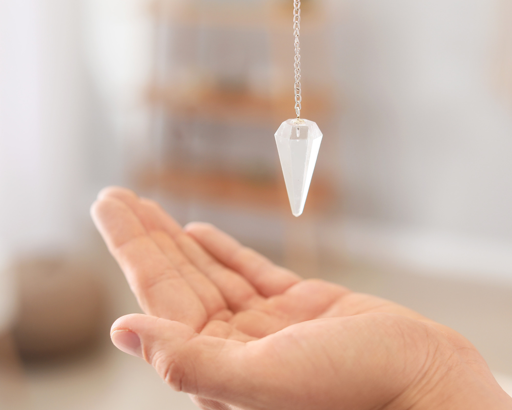 Hand holding a crystal pendulum used for energy healing and chakra alignment during a spiritual cleansing session.