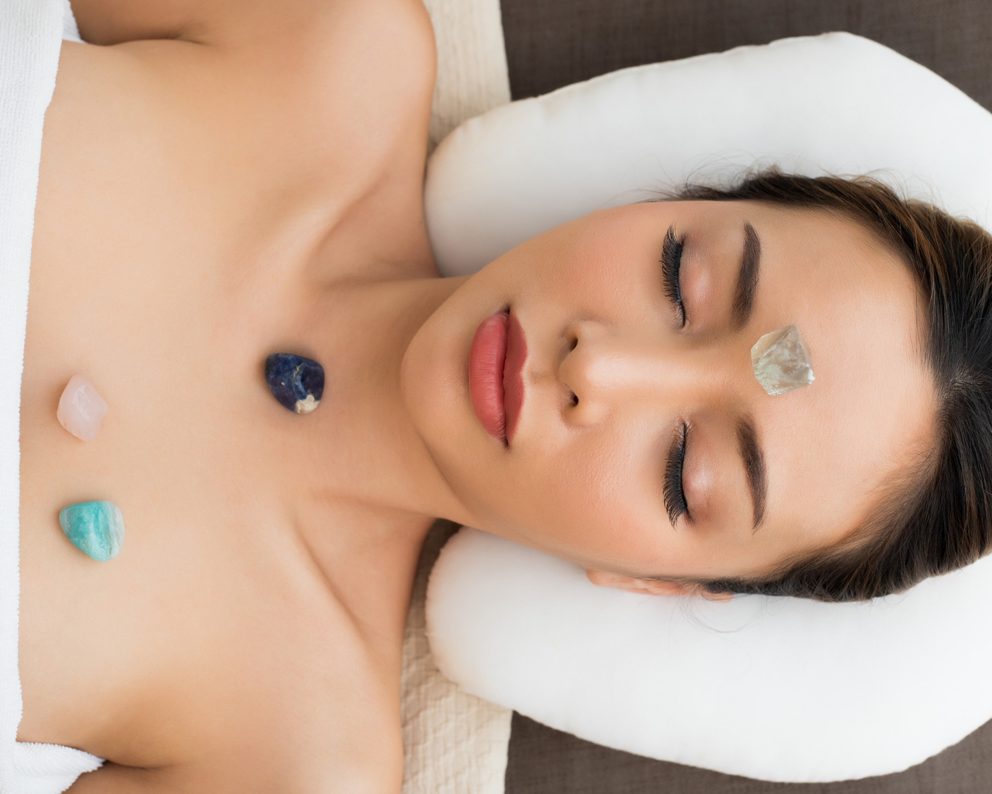 Woman lying down with eyes closed during a crystal healing session, with gemstones placed on her forehead, chest, and upper body for chakra balancing.
